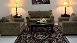 A living room with a brown sofa set, a coffee table with a floral centerpiece, and two lamps on side tables. - AlShowaish Apartments (Taif)