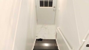 A staircase with a white door at the top, a pair of black shoes, and a pair of brown shoes at the bottom.