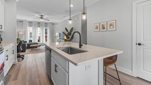 A modern kitchen with a central island, pendant lighting, and a view into the living area. - #StokeHotel: Boho Outdoorsy Vibes, Paddleboards, Kayak, Dog Park (Chattanooga)