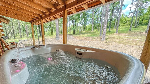 Een bubbelbad met stromend water, omringd door een houten pergola en uitzicht op een bos.