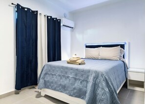 A bedroom with a bed, a nightstand, a wall-mounted air conditioner, and curtains. - Modern San Juan Apt w/ Parking Near Ocean Park (San Juan)
