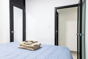 A room with a bed, two doors, and a stack of towels. - Modern San Juan Apt w/ Parking Near Ocean Park (San Juan)