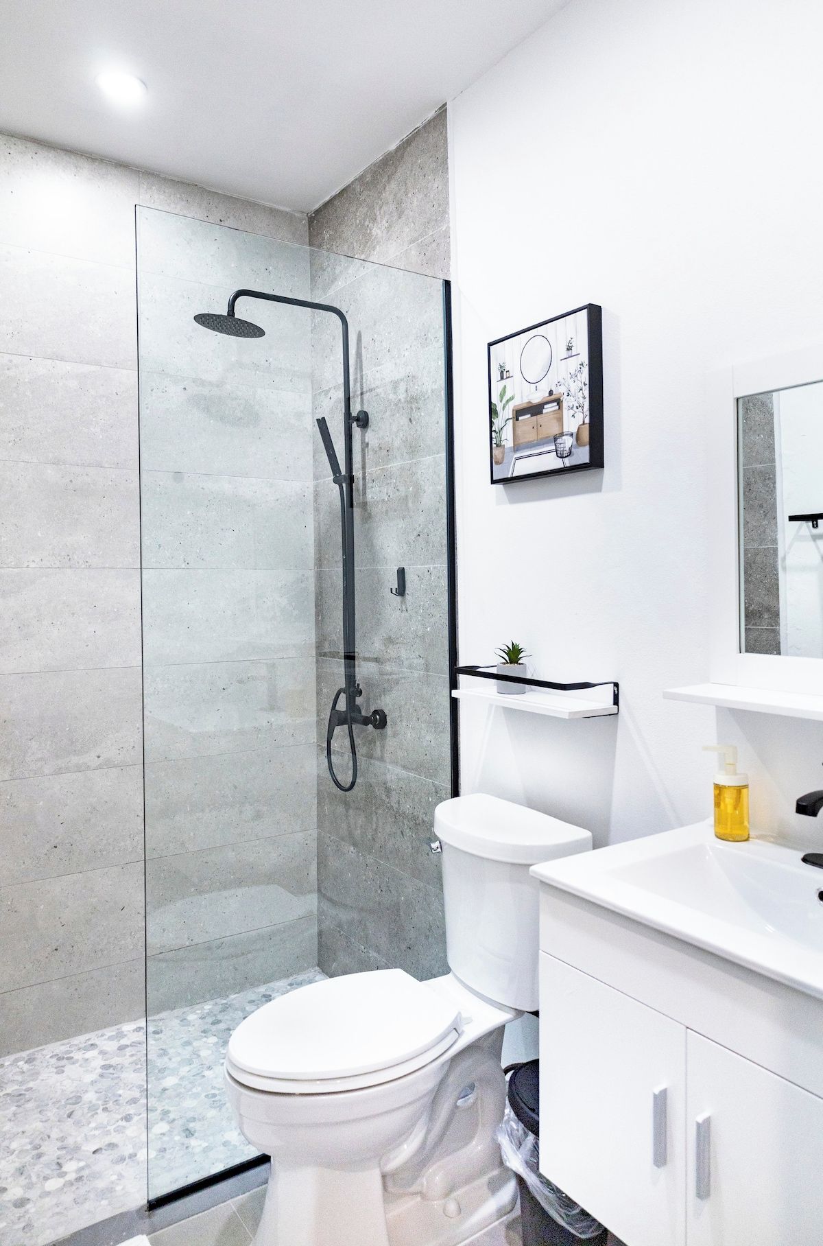 Un baño moderno con ducha envuelta en cristal, inodoro blanco y lavamanos con espejo.