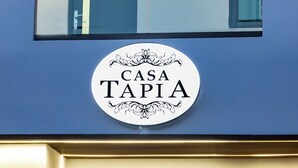 Ein rundes Schild mit dem Aufdruck 'CASA TAPIA' vor einer blauen Wand.