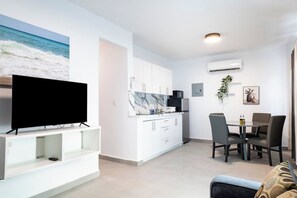 A modern living room with a flat-screen TV, a dining area with chairs and a table, and a kitchen with white cabinets and a marble backsplash. - Modern San Juan Apt w/ Parking Near Ocean Park (San Juan)