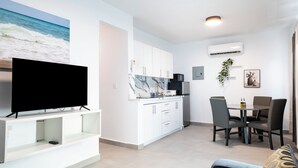 Ein modernes Wohnzimmer mit Flachbildfernseher, einem Essbereich mit Tisch und Stühlen sowie einer Küche mit weißen Schränken und einer Marmor-Spritzschutzwand.