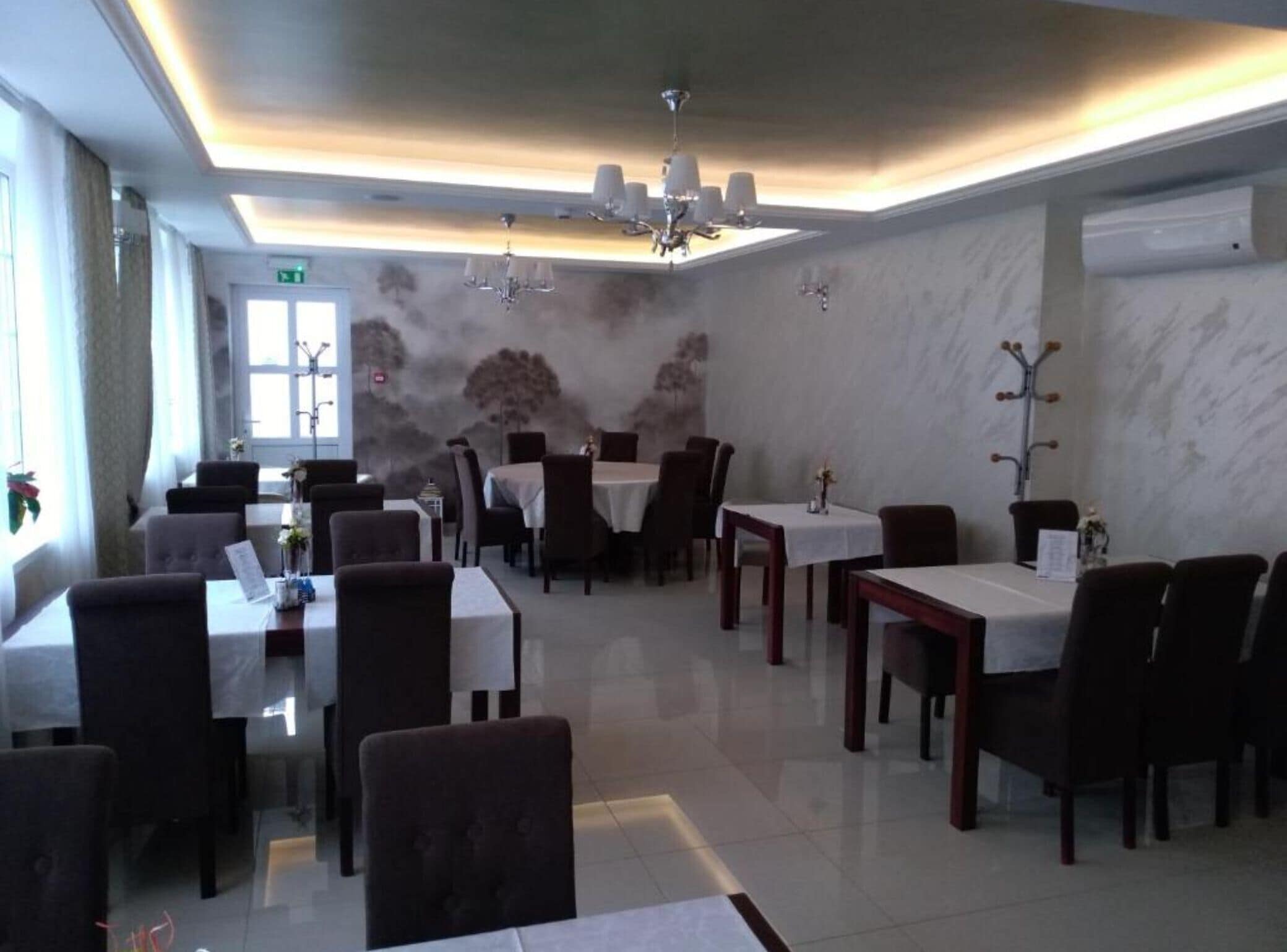 A restaurant with multiple tables and chairs, a chandelier, and a wall with a mural.