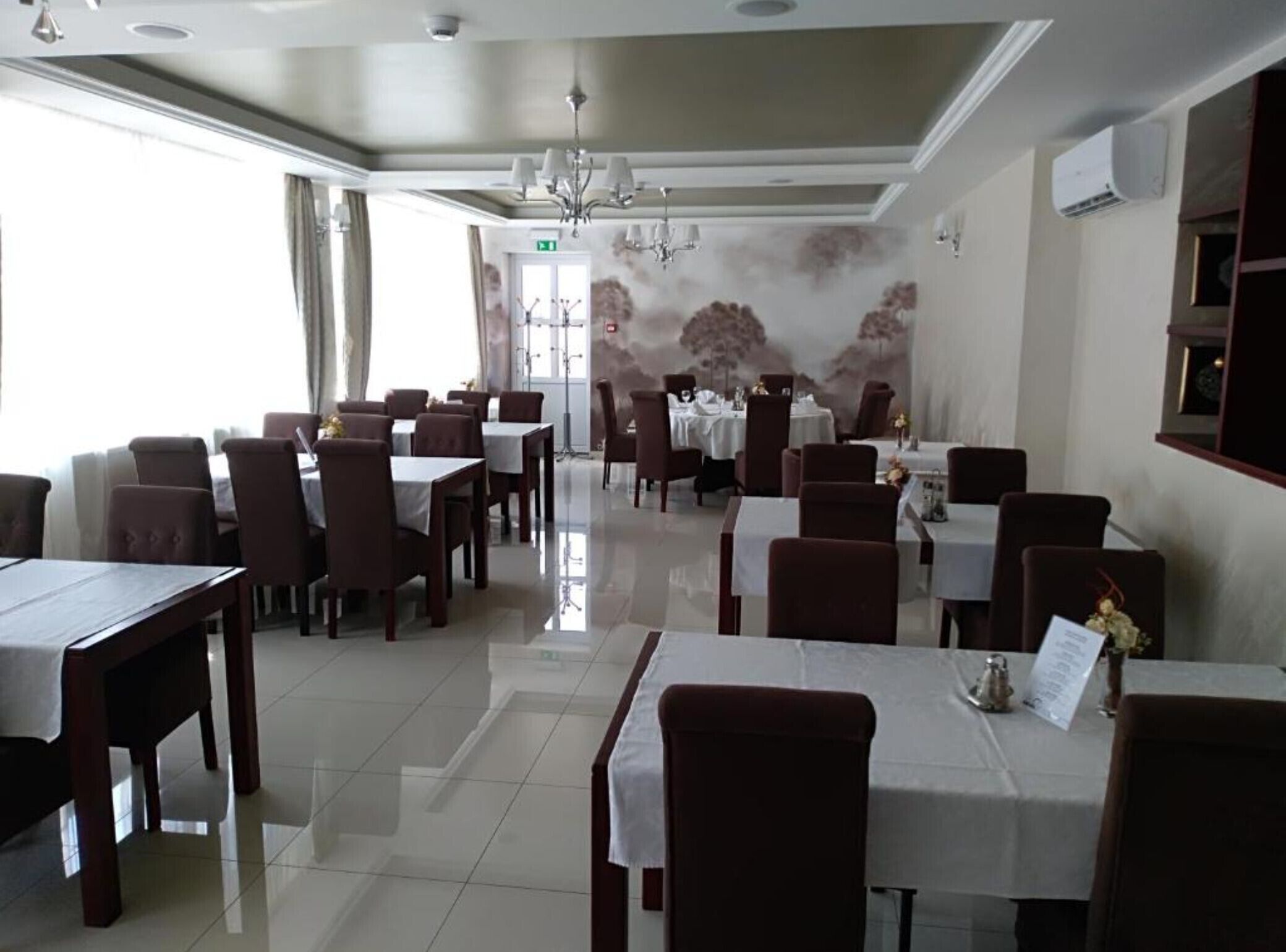 A restaurant with a modern interior, featuring a chandelier, white tablecloths, and a clean, tiled floor.