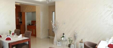 A dining area with a chandelier, tables set for dining, and a view into the kitchen.
