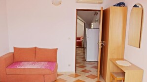 A small, compact room with a bed, a sofa, a wooden desk, and a wardrobe.