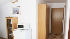 A room with a white refrigerator, a wooden cabinet with glass doors, a microwave on top of the refrigerator, and a wooden door.
