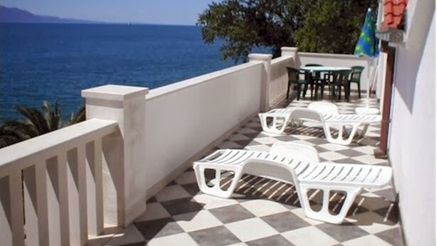 A balcony with white plastic chairs and a checkered floor, overlooking the sea.