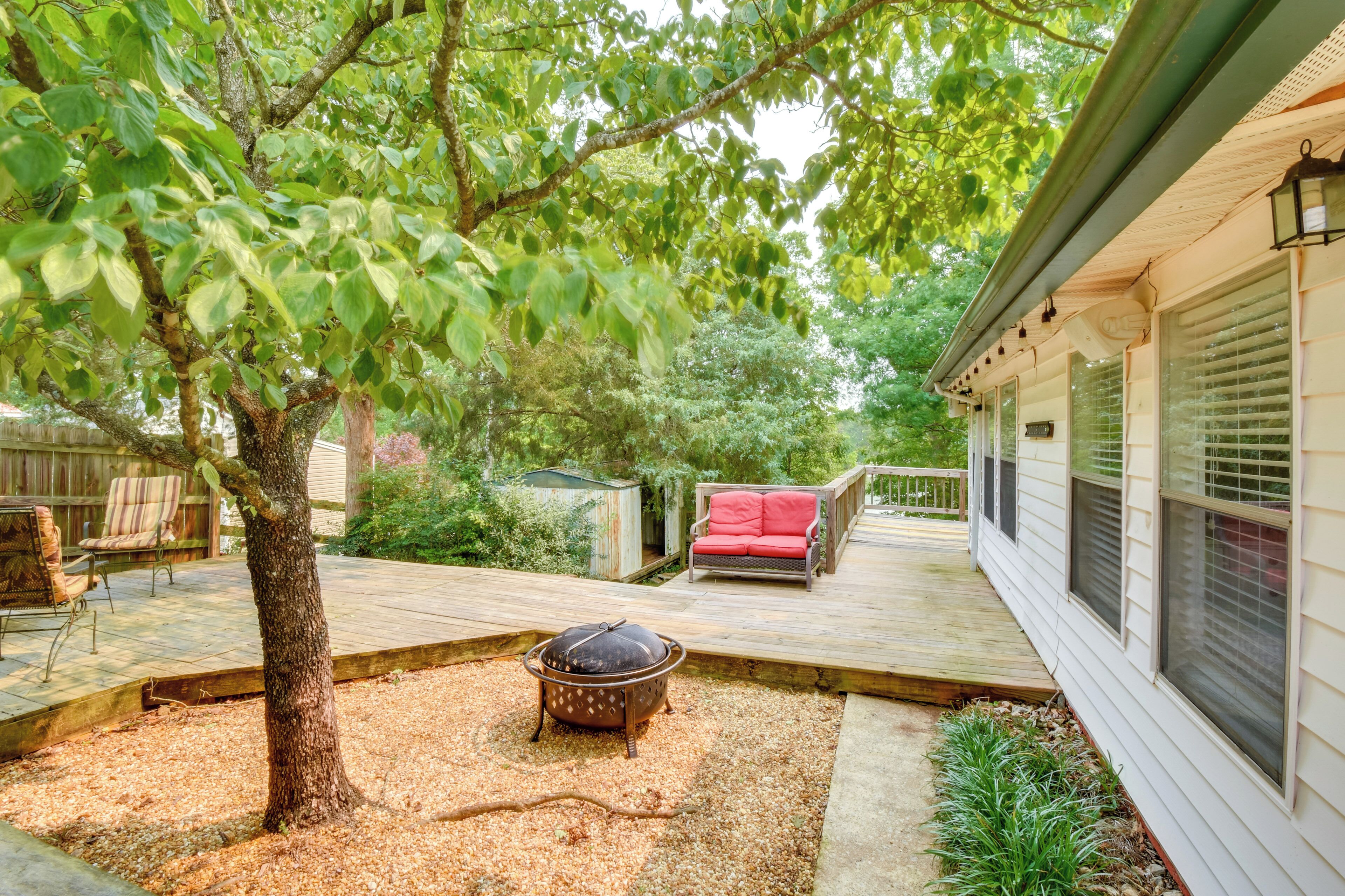 Een achtertuin met een houten terras, een barbecue, een rode buitenstoel en een kleine tuinhuis.