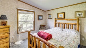 Ein Schlafzimmer mit einem hölzernen Bettgestell, einem Fenster, einer Holzkommode und einem Ventilator.