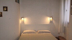 A simple, unadorned bedroom with a bed, two wall-mounted lights, and a wooden nightstand. - "Lovely Home" Cozy Bike Friendly Holiday Home with Wi Fi (Buonconvento)