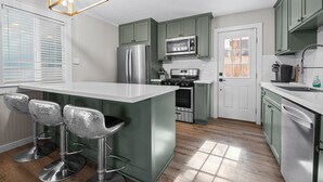 A kitchen with green cabinets, stainless steel appliances, and a central island with bar stools. - Brooklyn Cabins (Big Bear Lake)