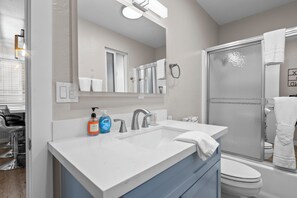Et moderne badeværelse med hvid vask, spejl, glasbrusekabine og toilet.
