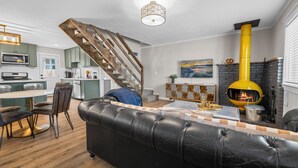 A modern kitchen with a wooden staircase, a black leather sofa, and a yellow wood stove. - Brooklyn Cabins (Big Bear Lake)