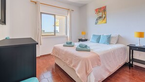 A bedroom with a bed, two bedside tables, a window with curtains, a painting on the wall, and a tiled floor. - Huniky 35 - Sea view, Wifi and air conditioning (Lagos)