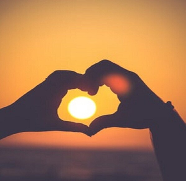 A silhouette of two hands forming a heart shape around a bright sun.