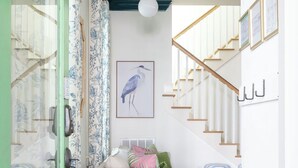 Ein Flur mit Treppe, einer Rattanbank, einem Bilderrahmen mit Vogelgemälde und einer grünen Tür.
