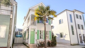 Ein zweistöckiges Haus mit grüner Tür und Fensterläden, einer kleinen Veranda und einer Palme im Vorgarten.