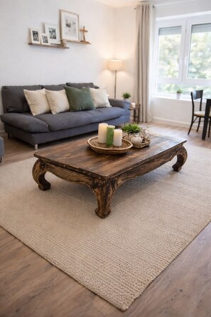 Un salon avec une table basse en bois rustique, un canapé gris et une grande fenêtre.