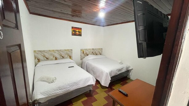 A small room with two beds, a TV mounted on the wall, and a colorful floor.