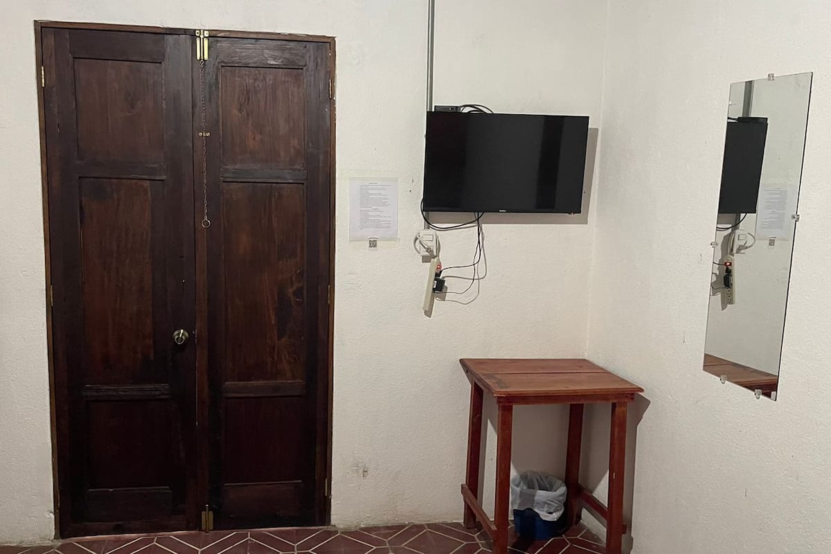 A room with a wooden door, a small wooden table, a wall-mounted TV, and a mirror.