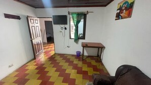 A room with a checkered floor, a television mounted on the wall, a window with a curtain, and a door leading to another room.