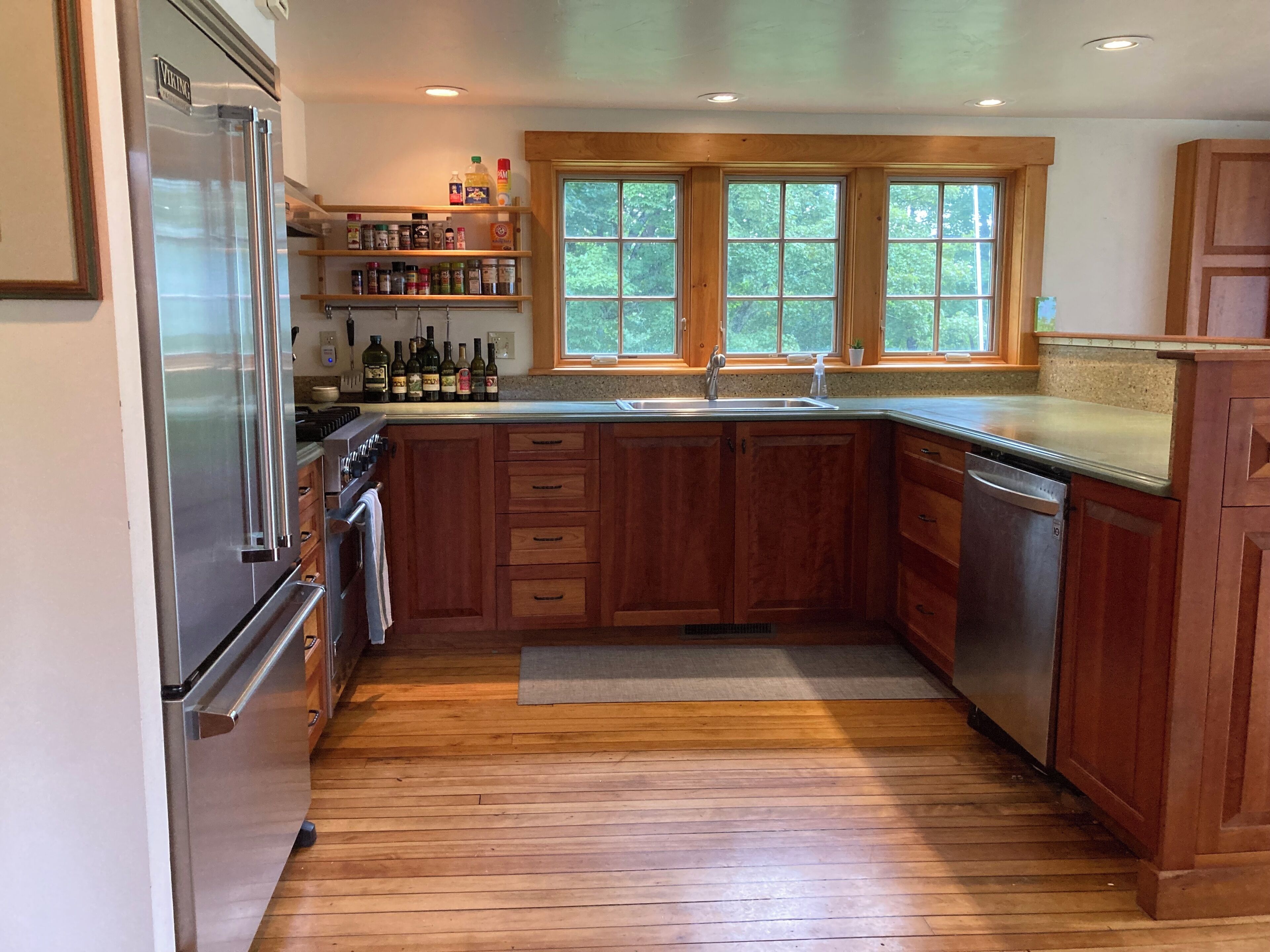 A kitchen with wooden cabinets, a stainless steel refrigerator, and a window above the sink.