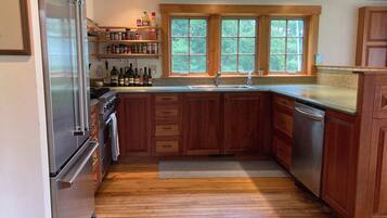 A kitchen with wooden cabinets, a stainless steel refrigerator, and a window above the sink.