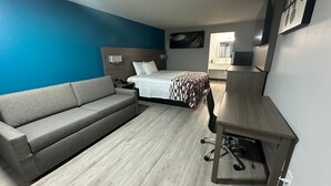 Una habitación de hotel con un sofá gris, una cama con manta de cuadros, un escritorio de madera y un espejo.
