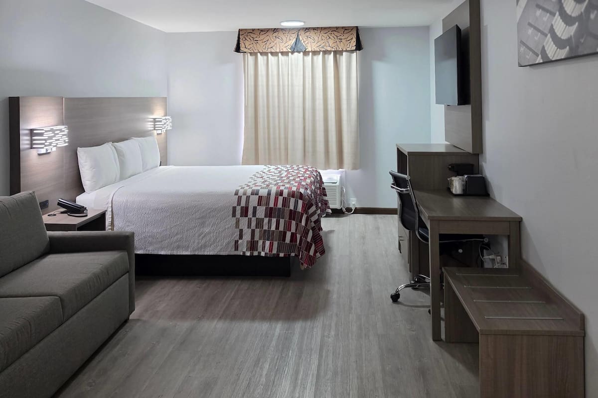 Una habitación de hotel con cama, escritorio, silla, televisor y ventana con cortinas.