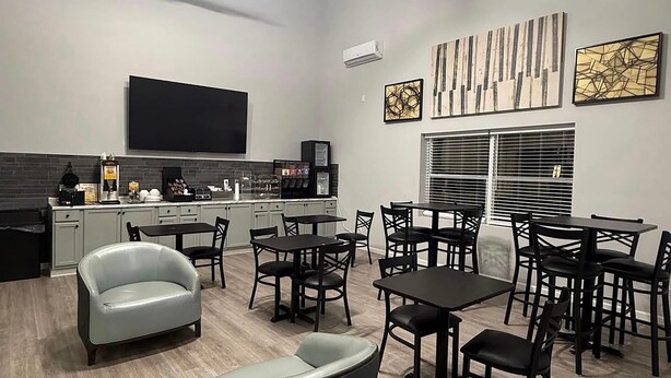 Una cocina moderna con televisor de pantalla plana, cafetera y comedor con varias mesas y sillas.