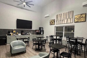 Una cocina moderna con televisor de pantalla plana, cafetera y comedor con varias mesas y sillas.