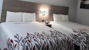 A hotel room with two beds, a headboard, a nightstand, and a wall-mounted light fixture.