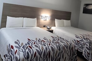 Ein Hotelzimmer mit zwei Betten, einem Kopfteil, einem Nachttisch und einer an der Wand befestigten Leuchte.