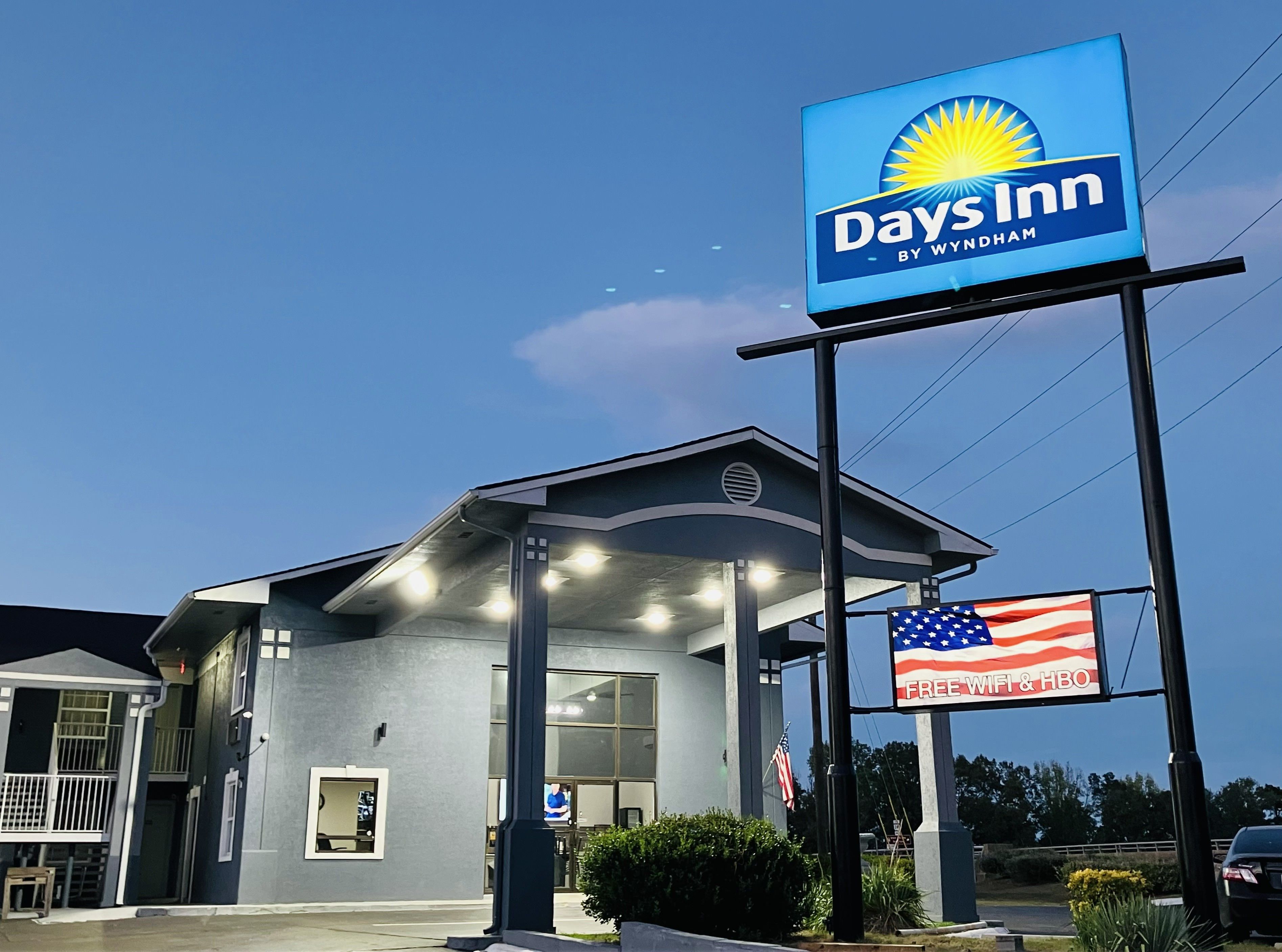 A Days Inn by Wyndham with a clear sky, an American flag, and a sign indicating free WiFi & HBO.