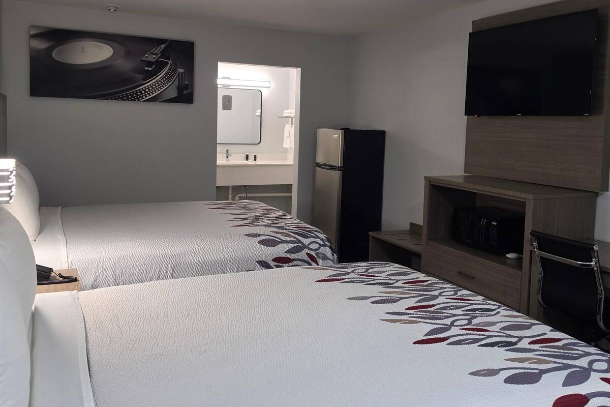 Habitación de hotel con dos camas, televisión, refrigerador, microondas y espejo de baño.