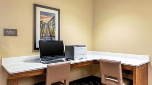 Un centro de negocios con un escritorio, dos sillas, una computadora portátil, una impresora y un cuadro con una imagen de un puente.