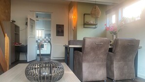 A modern dining area with a round table, two cushioned chairs, a wicker pendant light, and a view of the kitchen in the background. - Vacation home near the beach and the cities of Amsterdam and Haarlem. (Beverwijk)
