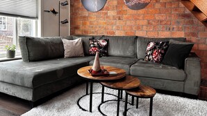 A modern living room with a grey sectional sofa, a round wooden coffee table, and a brick wall with two circular wall art pieces. - Vacation home near the beach and the cities of Amsterdam and Haarlem. (Beverwijk)