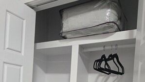 Un armario blanco con puertas abiertas, mostrando estantes y una barra para colgar ropa.