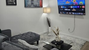 Una sala de estar moderna con un sofá gris, un televisor de pantalla plana montado en la pared y un jarrón decorativo sobre una mesa de centro.