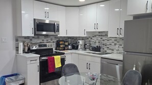 Una cocina moderna con armarios blancos, electrodomésticos de acero inoxidable y una mesa de comedor de vidrio con sillas.