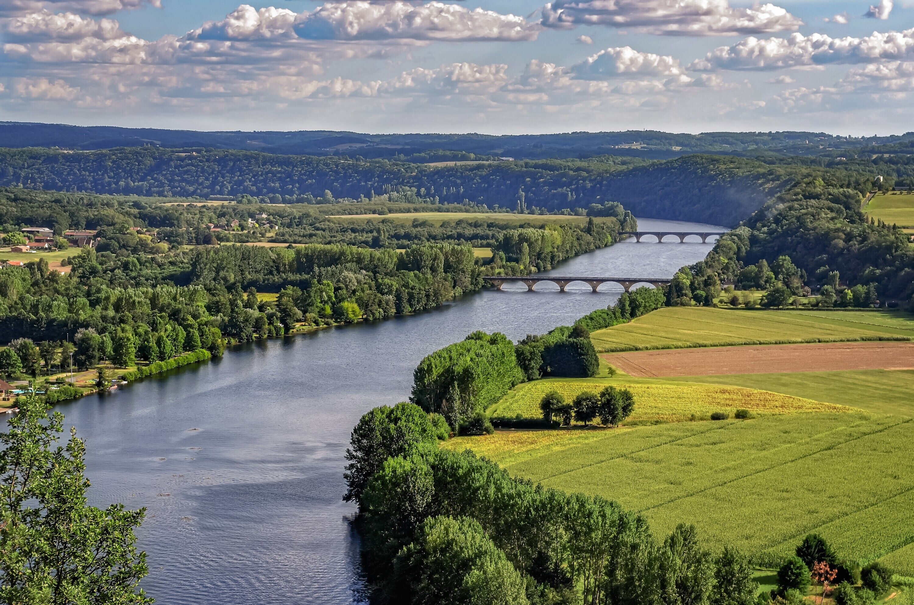 A river with a bridge, green fields, and distant hills.