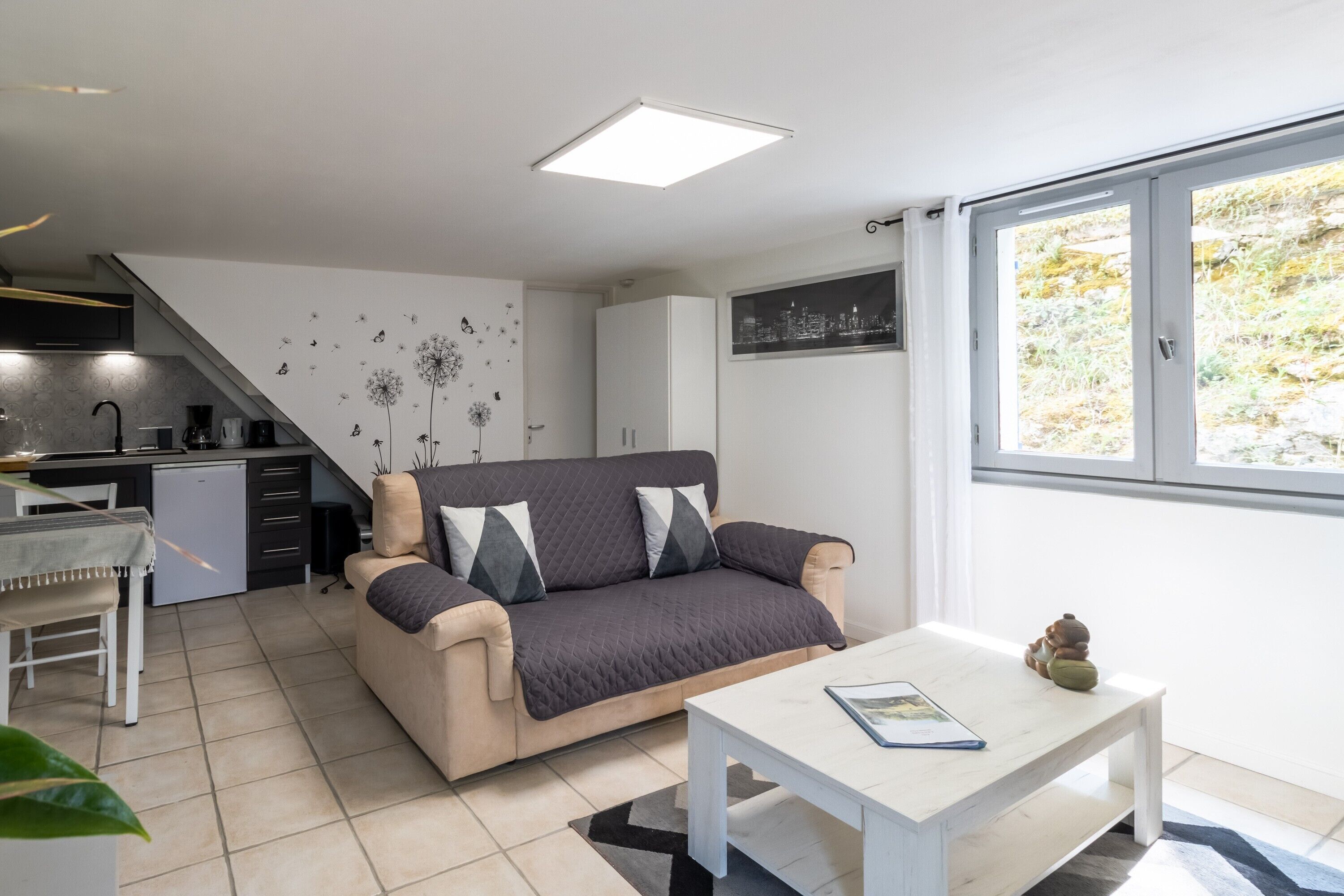 Een moderne woonkamer met een bank, een eettafel, een keuken en een groot raam.