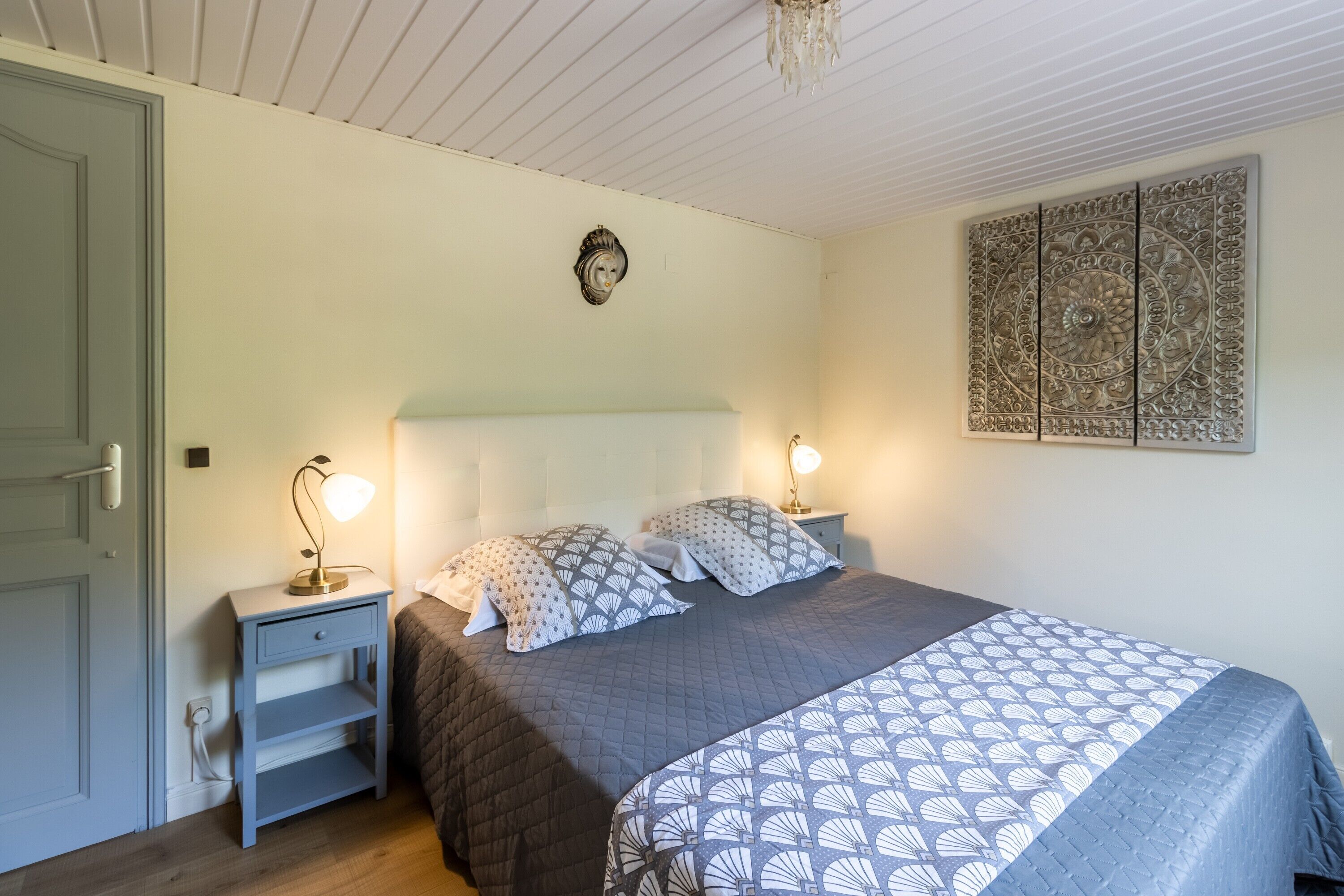 A bedroom with a bed, bedside tables, a wall clock, and a decorative panel.