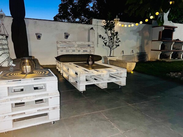 Eine Terrasse im Freien mit einem weißen Holztisch und -stühlen, einem dekorativen Laternen und Lichterketten.